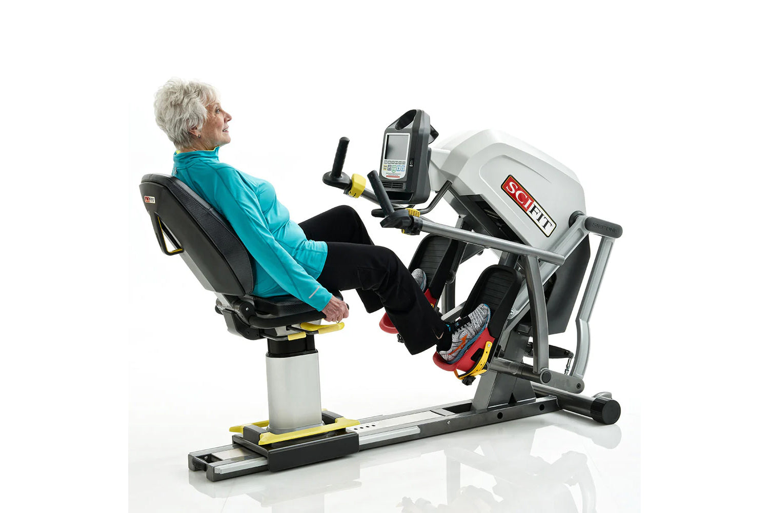 Older woman in turquoise jacket using white and black SCIFIT recumbent stepper with digital display, handlebars and foot peda