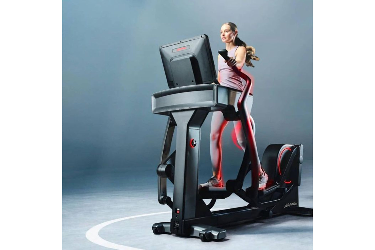 Woman wearing burgundy and white athletic leggings using Life Fitness Symbio incline elliptical with digital display against 