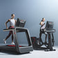 Two models demonstrating Life Fitness Symbio incline elliptical machines with black frames, digital screens, and red accent d