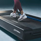 Person wearing burgundy cropped leggings and white mesh running shoes jogging on a black Life Fitness treadmill with blue acc