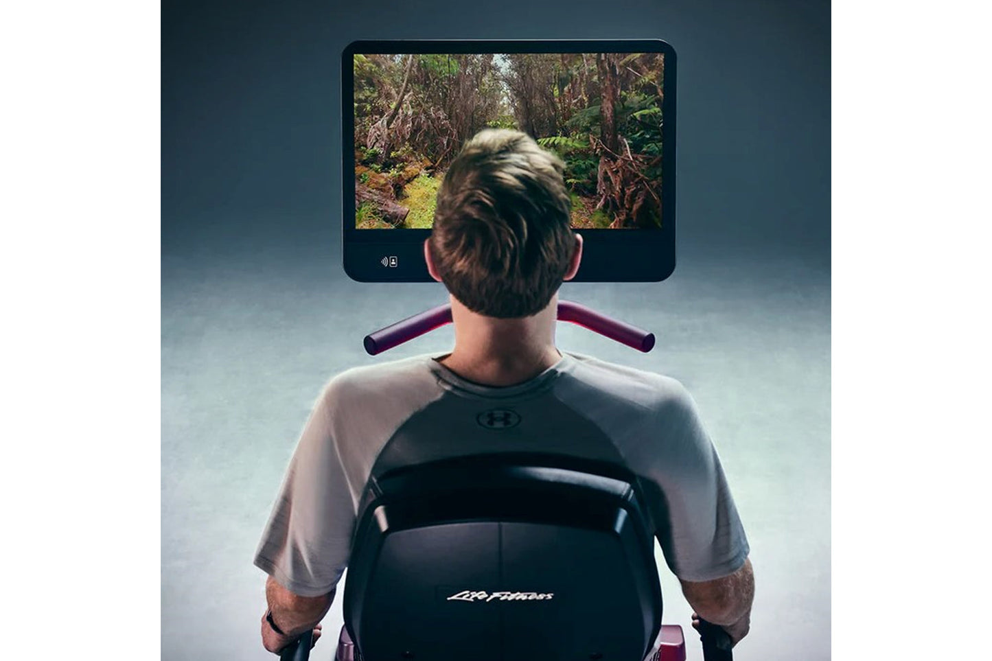 Person using Life Fitness Symbio recumbent cycle with forest trail displayed on screen, viewed from behind