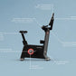 Black stationary exercise bike with labeled features including micro controls, seat adjustment sensor, dual performance pedal