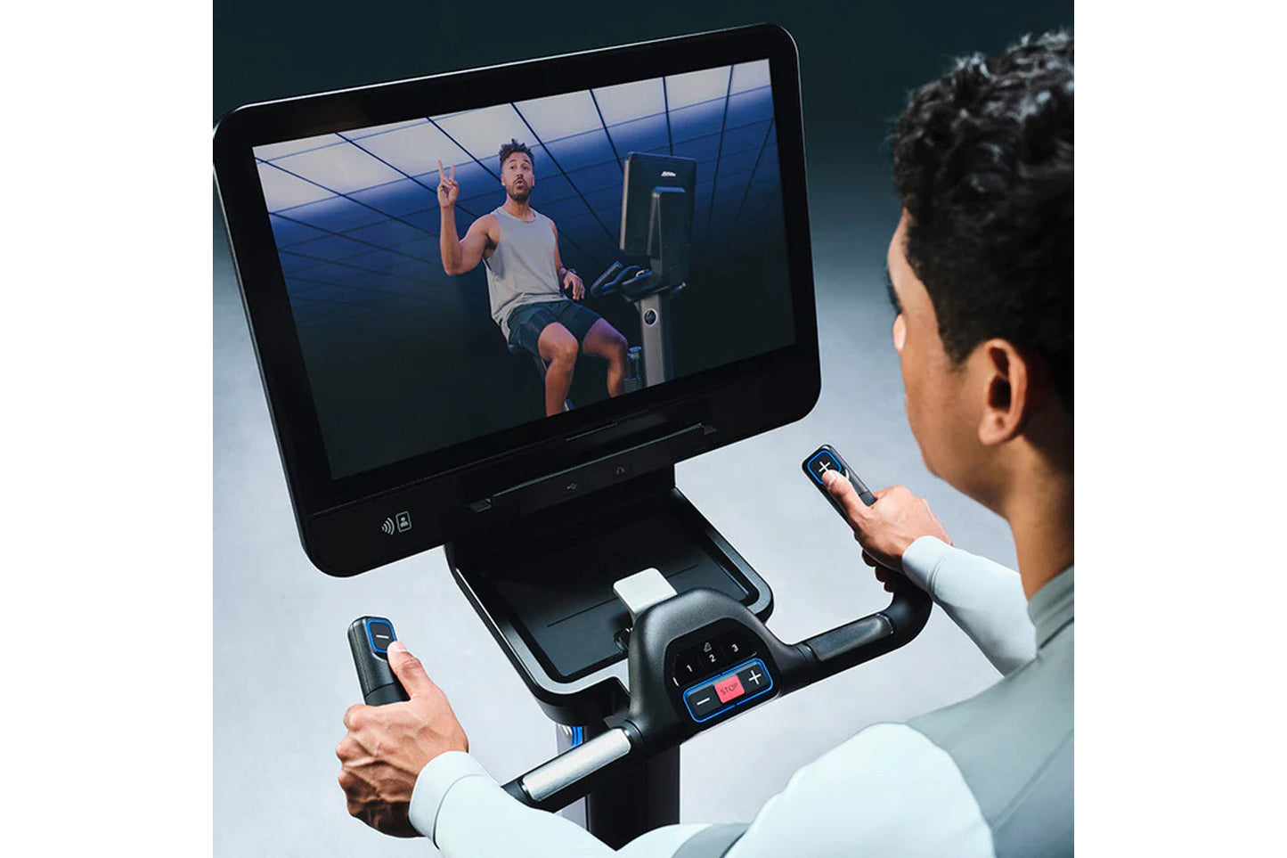 Person using Life Fitness Symbio Switch stationary exercise bike with touchscreen display showing workout video and handheld 