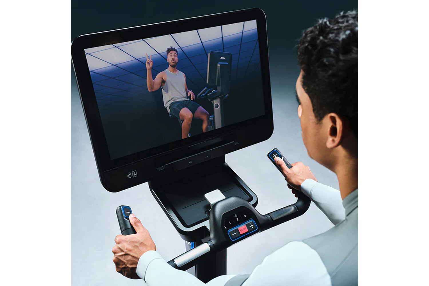 Person using Life Fitness Symbio Switch stationary exercise bike with touchscreen display showing workout video and handheld 