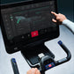 User interacting with Life Fitness Symbio Switch stationary bike, displaying digital dashboard with fitness metrics and teal-