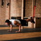 Man performing suspended plank exercise using red and black pull-up assist straps in gym with brick wall background