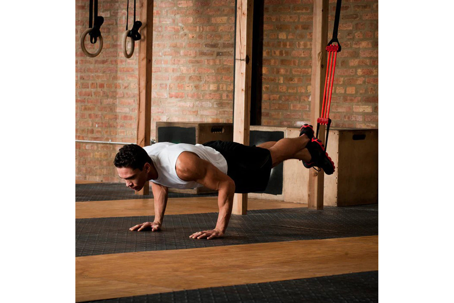 Man performing suspended plank exercise using red and black pull-up assist straps in gym with brick wall background
