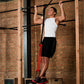 Man performing pull-up on bar using red resistance band assistance in gym with brick wall background