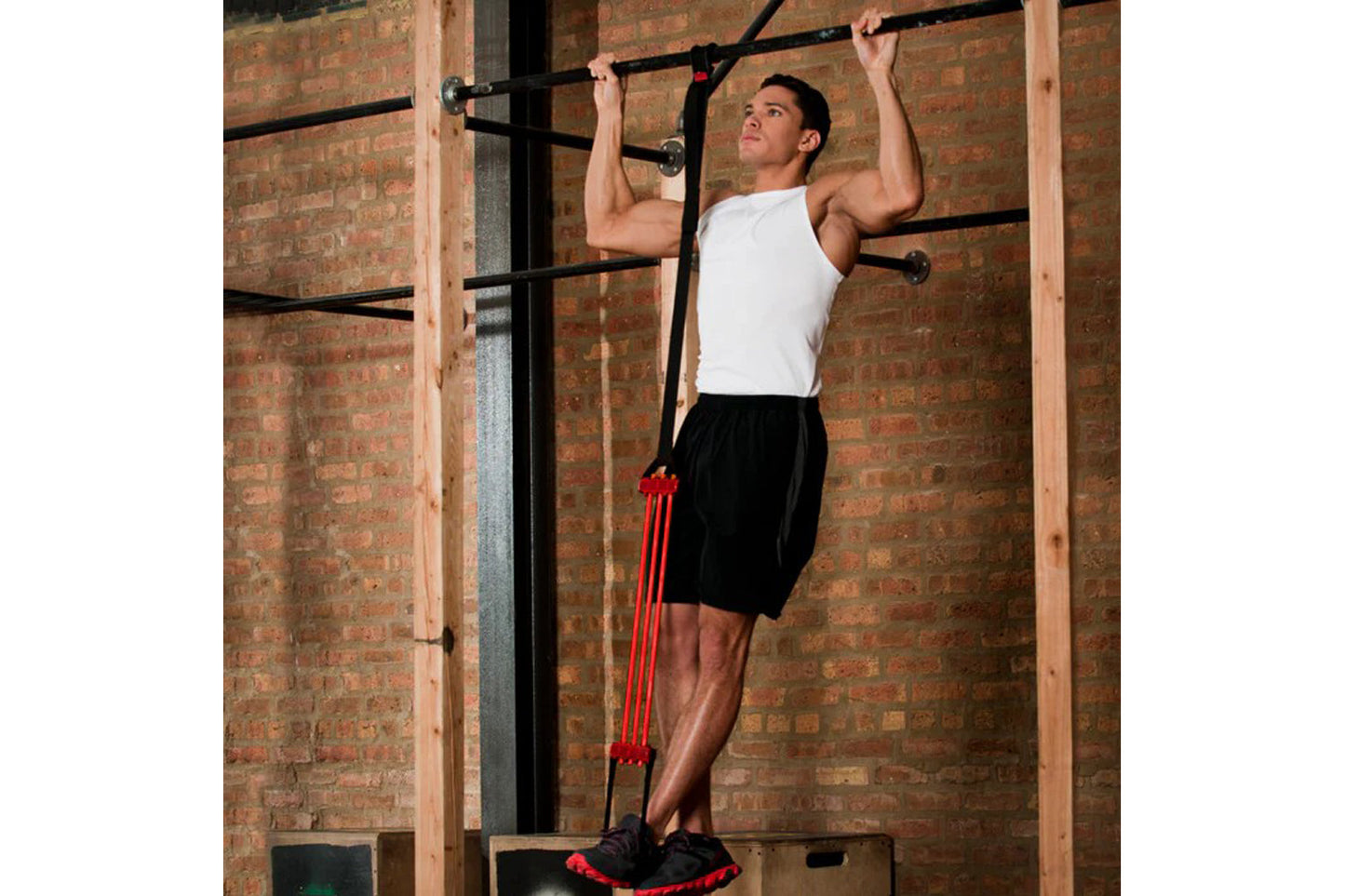 Man performing pull-up on bar using red resistance band assistance in gym with brick wall background
