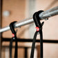 Black pull-up assist band with red buckle clipped to metal pull-up bar, showing elastic resistance strap