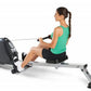 Woman using black and gray LifeSpan RW1000 indoor rowing machine, wearing green tank top and black shorts