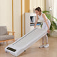 Woman in white athletic wear using white under-desk treadmill with black digital display in home office setting