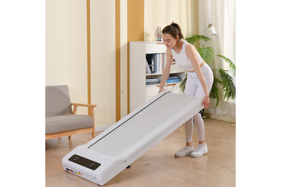 Woman in white athletic wear using white under-desk treadmill with black digital display in home office setting