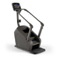 Black stair climbing exercise machine with digital touchscreen console, dual handrails with gold accents, and stepping platfo