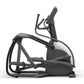 Black and gray Matrix elliptical machine with dual handles and foot pedals on white background