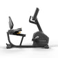 Matrix Endurance recumbent exercise bike with black frame, padded seat, digital display, and adjustable handlebars on white b
