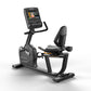 Matrix black recumbent exercise bike with digital touchscreen console displaying workout content, padded seat with backrest, 