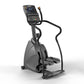 Black and gray commercial stepper machine with digital display console, handles, and foot pedals on white background