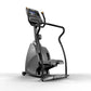 Black and gray commercial stepper exercise machine with digital display console, handlebar, and footrest on white background