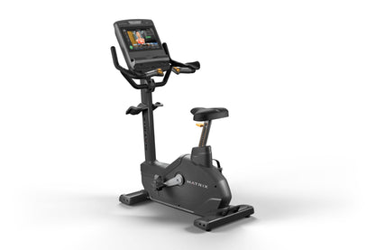 Matrix Endurance upright exercise bike with black frame, digital display console, dual handles, and black padded seat on whit