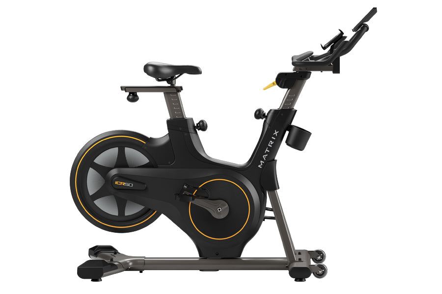 Black and gold Matrix ICR50 indoor cycling bike with adjustable handlebars and seat, viewed from the side on white background