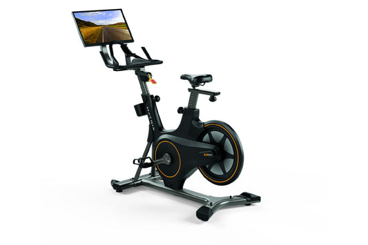 Black stationary exercise bike with orange accents, tablet console mounted on handlebar displaying road scenery, on white bac