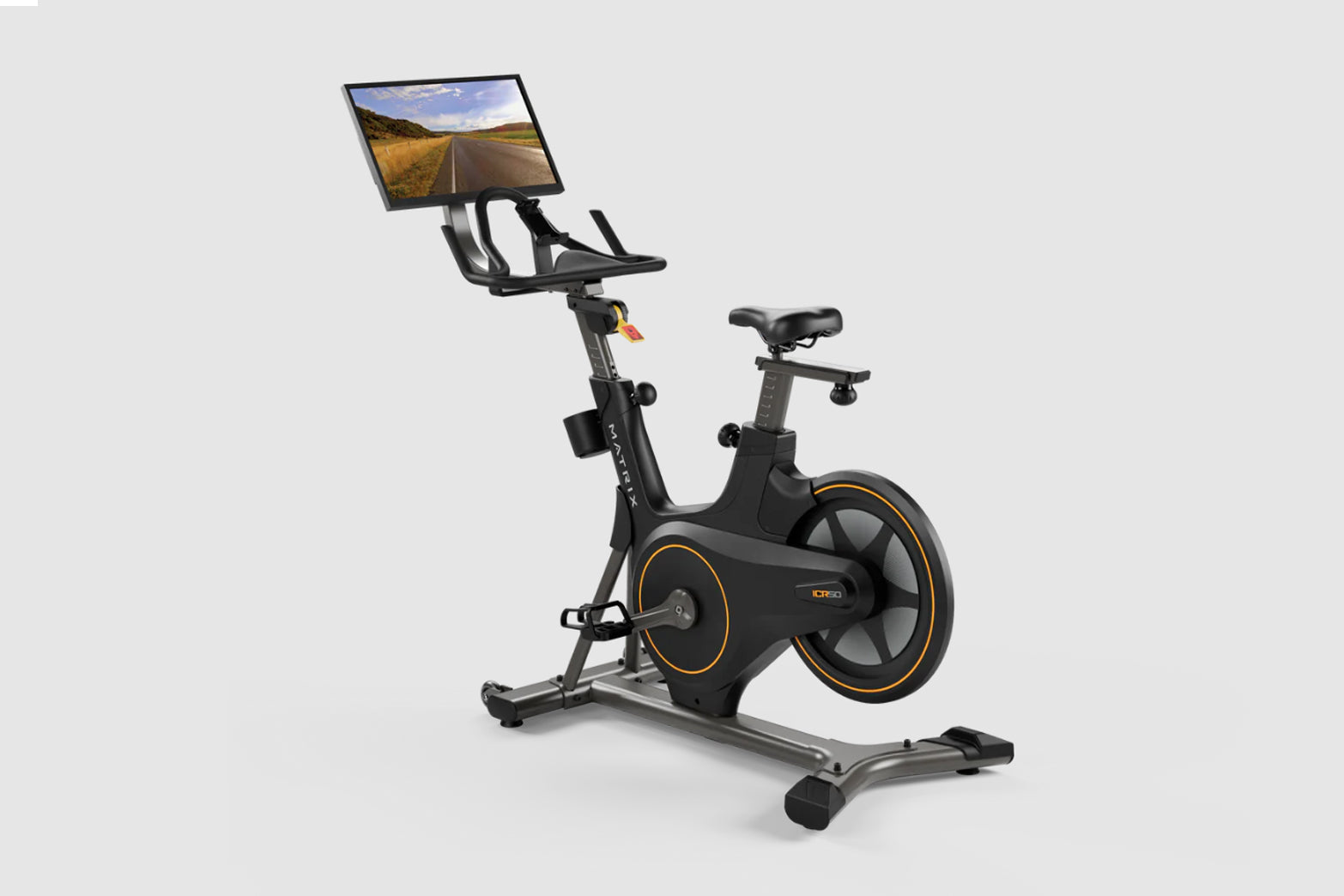 Black and gold stationary exercise bike with interactive monitor displaying desert road scene, on white background