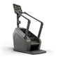 Black and gray stair climbing machine with digital display, handrails, and textured foot pedals on white background