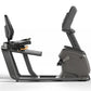 Matrix Lifestyle recumbent exercise bike with charcoal frame, padded seat, and adjustable backrest on white background