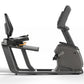 Matrix Lifestyle dark gray recumbent exercise bike with padded seat, adjustable backrest, and digital display on white backgr