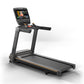 Black Matrix treadmill with gray running deck, gold accents, and digital touchscreen display mounted on uprights showing vide