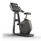 Black upright stationary exercise bike with digital display console, handlebars, padded seat, and stabilized base on white ba