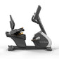 Matrix black and gray recumbent exercise bike with digital display and adjustable seat, shown from side angle on white backgr