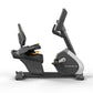 Matrix gray and white recumbent exercise bike with black seat, dual handles, and digital display on white background