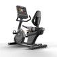 Matrix black and gray recumbent exercise bike with digital touchscreen display and padded seat on white background