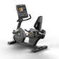 Black and gray Matrix recumbent exercise bike with digital display screen, padded seat, and foot pedals on white background