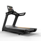 Black commercial treadmill with digital console display, orange accent stripe, and dual handrails on white background