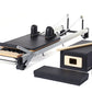 Merrithew SPX Home Pilates Reformer with black platform, wooden footbar, dual black domes, white frame, and included accessor