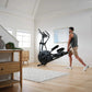 Man using black NordicTrack AirGlide 16 elliptical machine in modern home gym with wood furniture