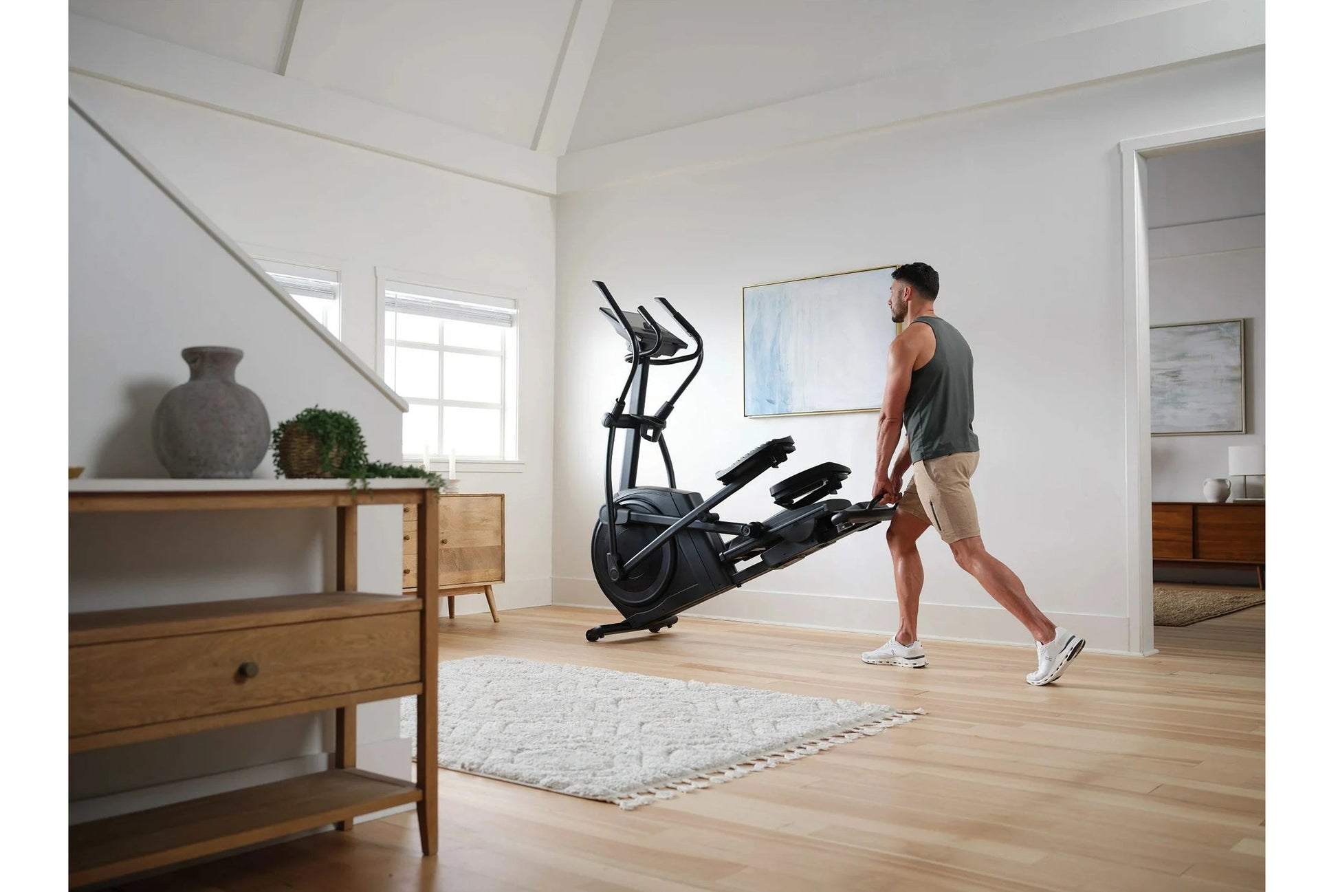 Man using black NordicTrack AirGlide 16 elliptical machine in modern home gym with wood furniture
