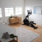 Black elliptical machine with tablet holder and dual handles in bright home gym with wooden floor and natural light