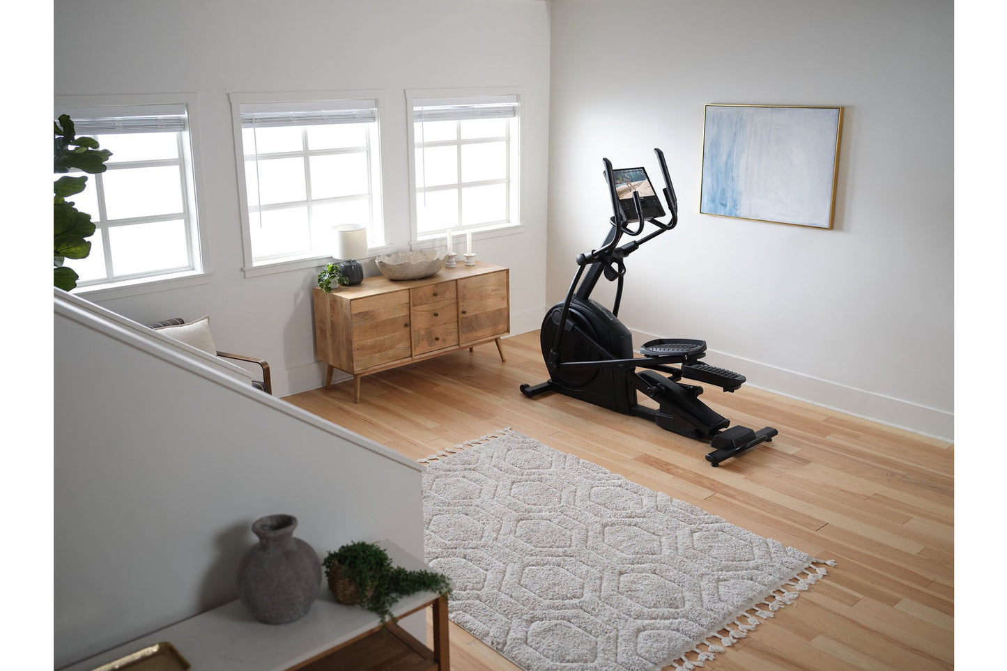 Black elliptical machine with tablet holder and dual handles in bright home gym with wooden floor and natural light