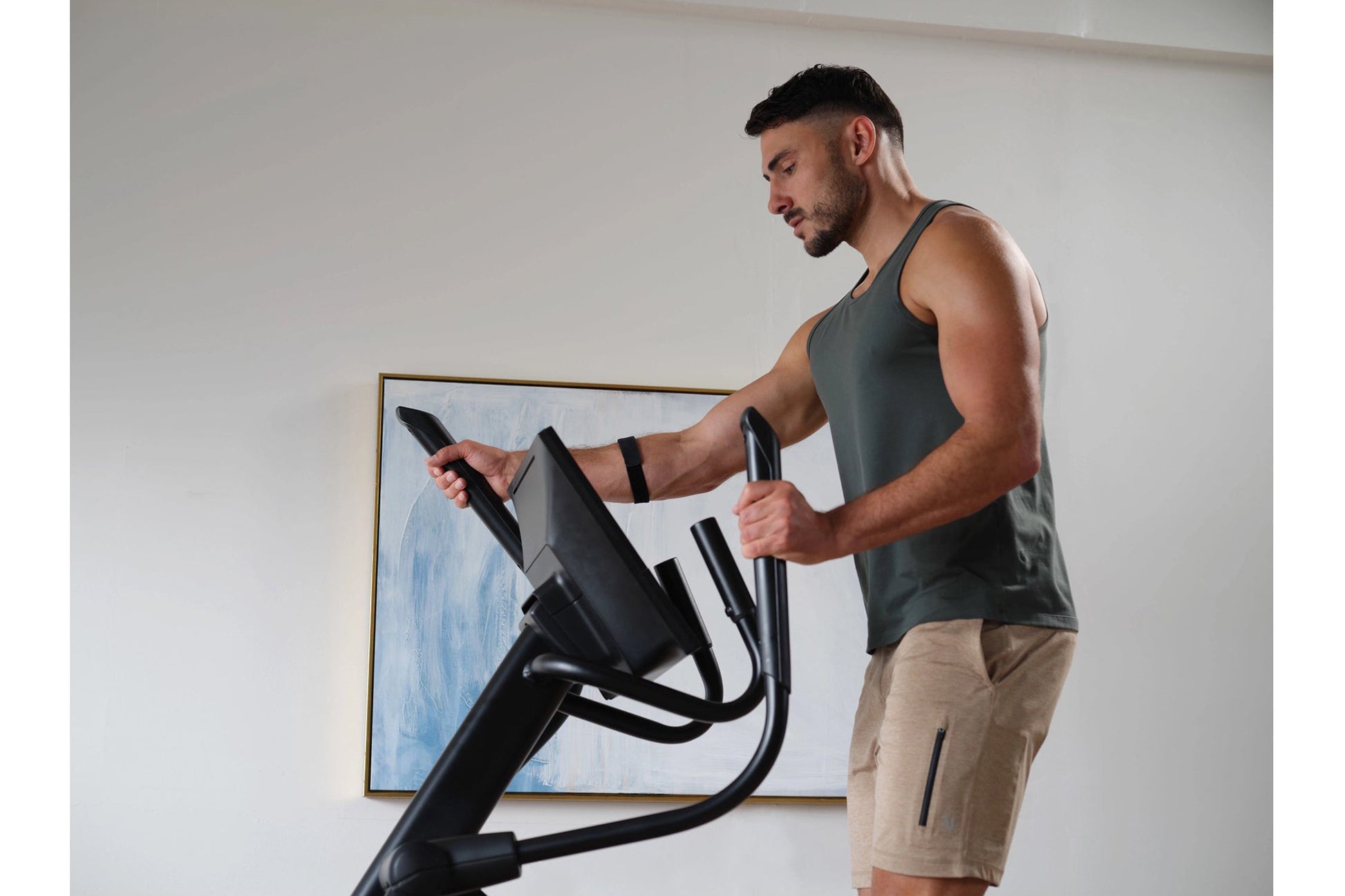 Man wearing charcoal tank top using black NordicTrack AirGlide 16 elliptical machine indoors