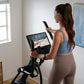 Woman wearing blue sports bra and tan leggings using black NordicTrack AirGlide 16 elliptical with digital display in home gy