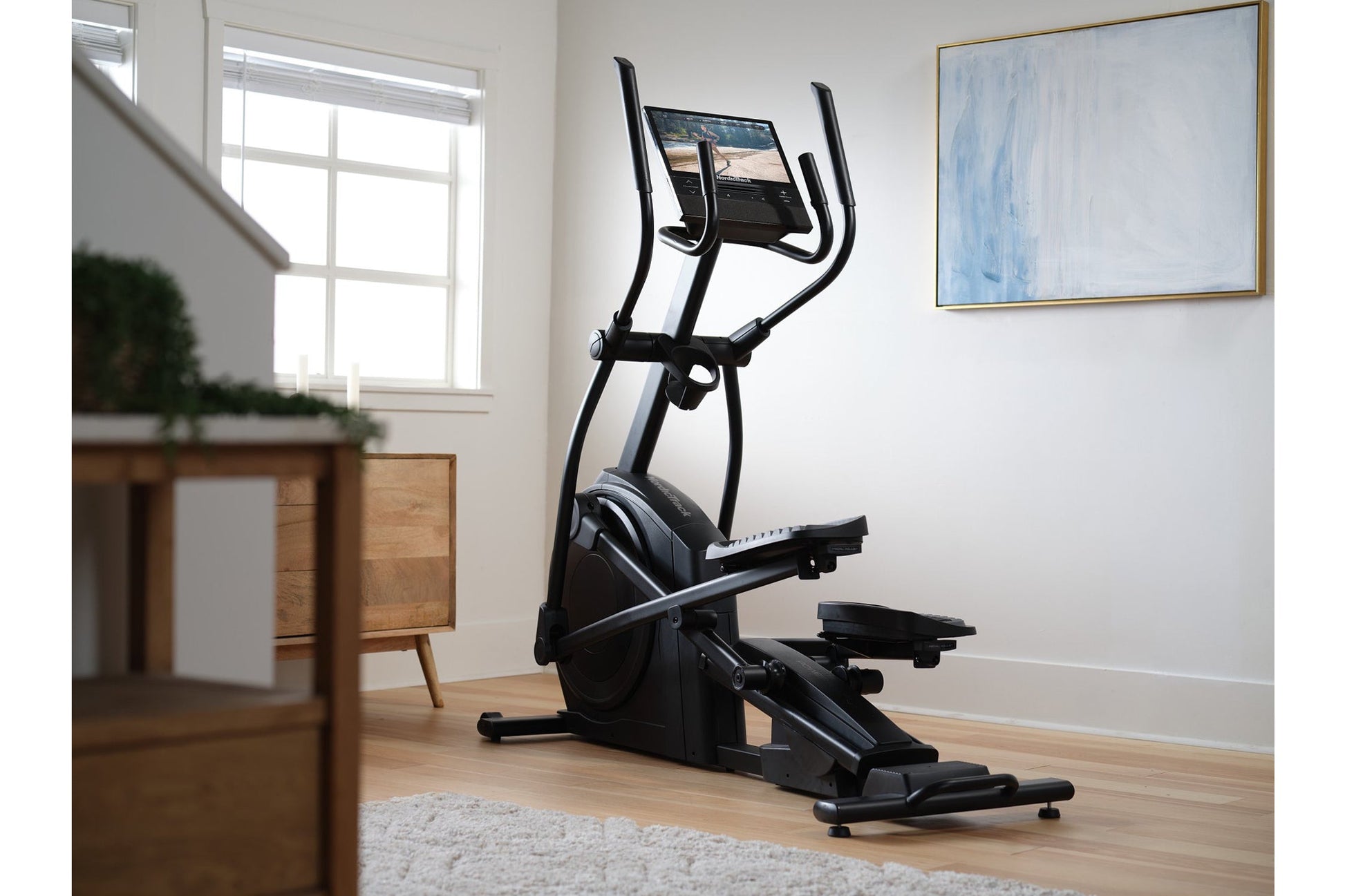 Black elliptical machine with digital screen and dual handles in modern living room setting