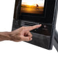Hand touching touchscreen display on black NordicTrack recumbent exercise bike showing cyclist at sunset