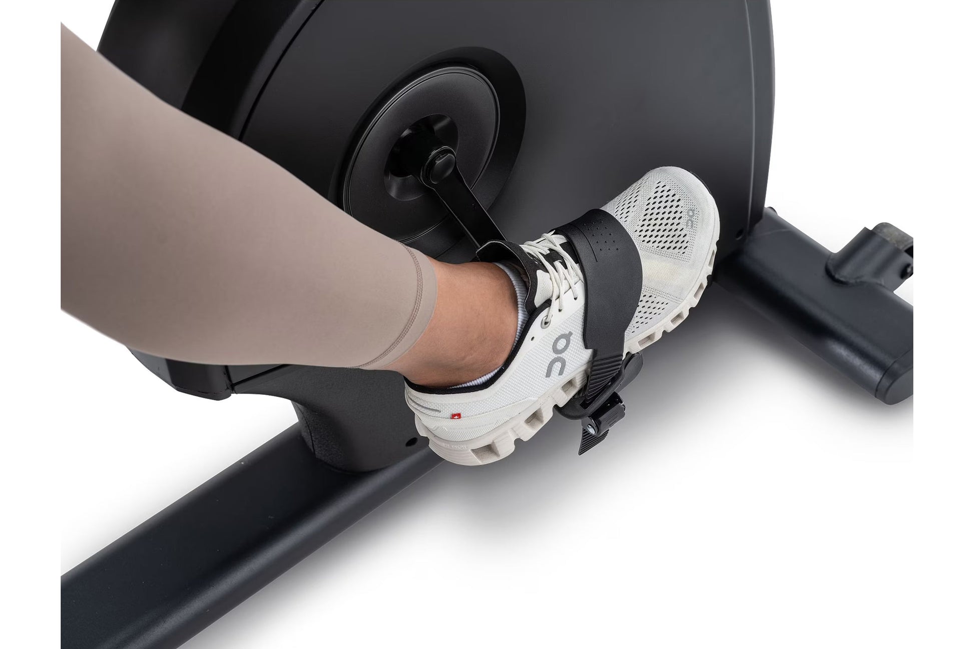 Foot on white and black sneaker on NordicTrack recumbent exercise bike pedal, worn by model in beige leggings