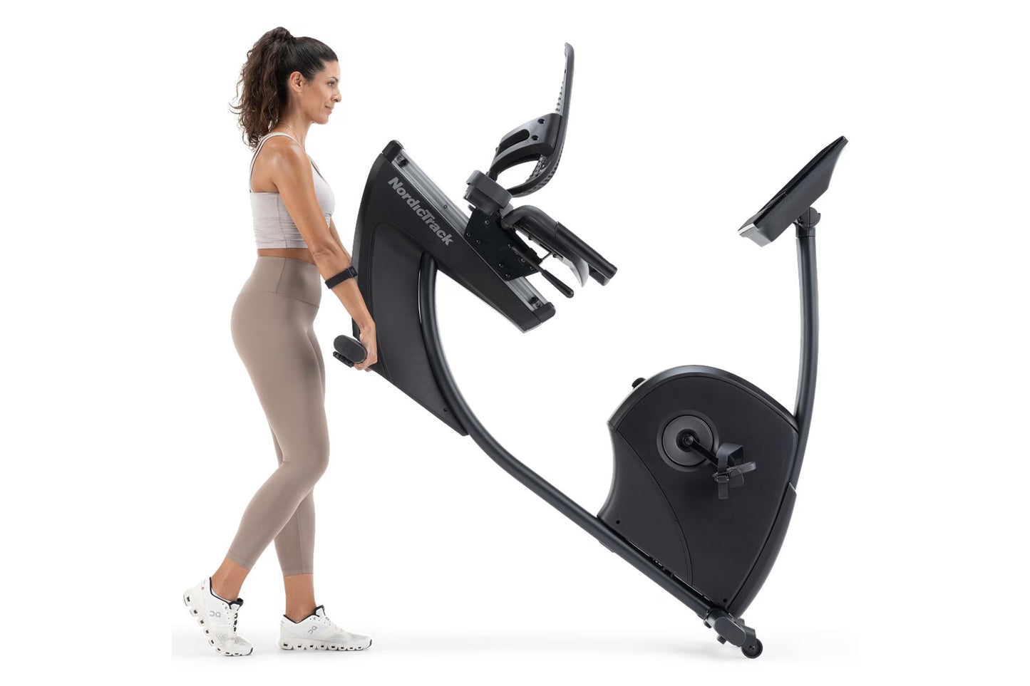 Woman using black NordicTrack recumbent exercise bike with digital display and adjustable seat, shown from side view on white