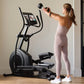 Woman wearing light pink workout set exercising on black NordicTrack elliptical machine with digital display in home gym