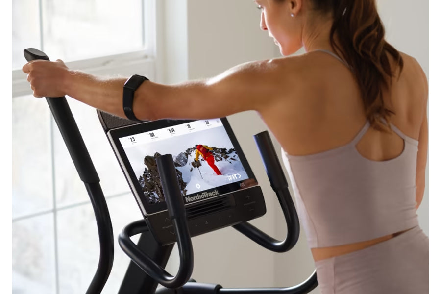 Woman wearing lavender sports bra using NordicTrack AirGlide 14i elliptical with digital display screen showing workout metri